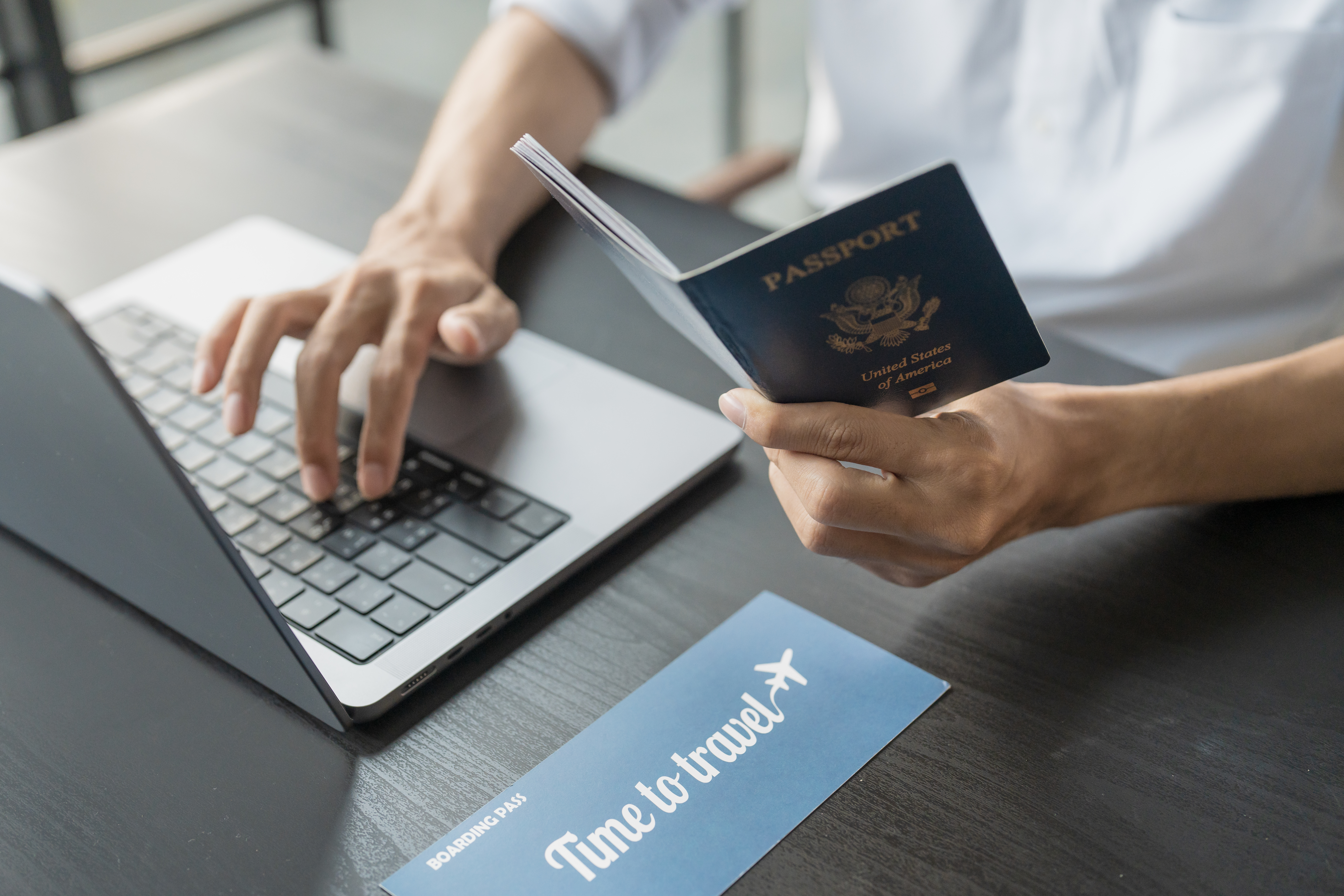 Hand Man Online booking and buying plane tickets using laptop phone and credit card Planning trip travel vacation with passport and ticket
