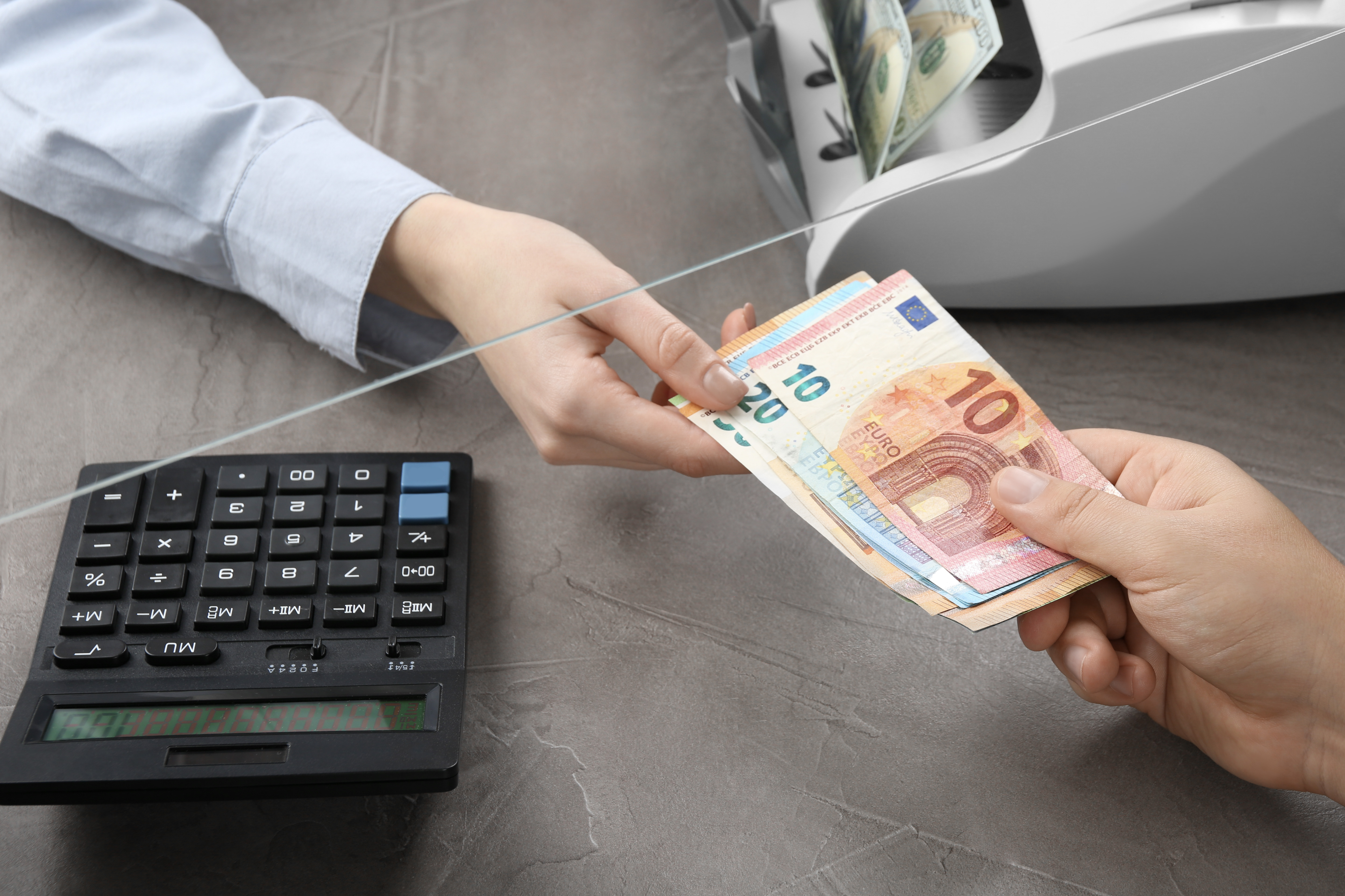 Client giving euro banknotes to cashier at table in money exchange, closeup