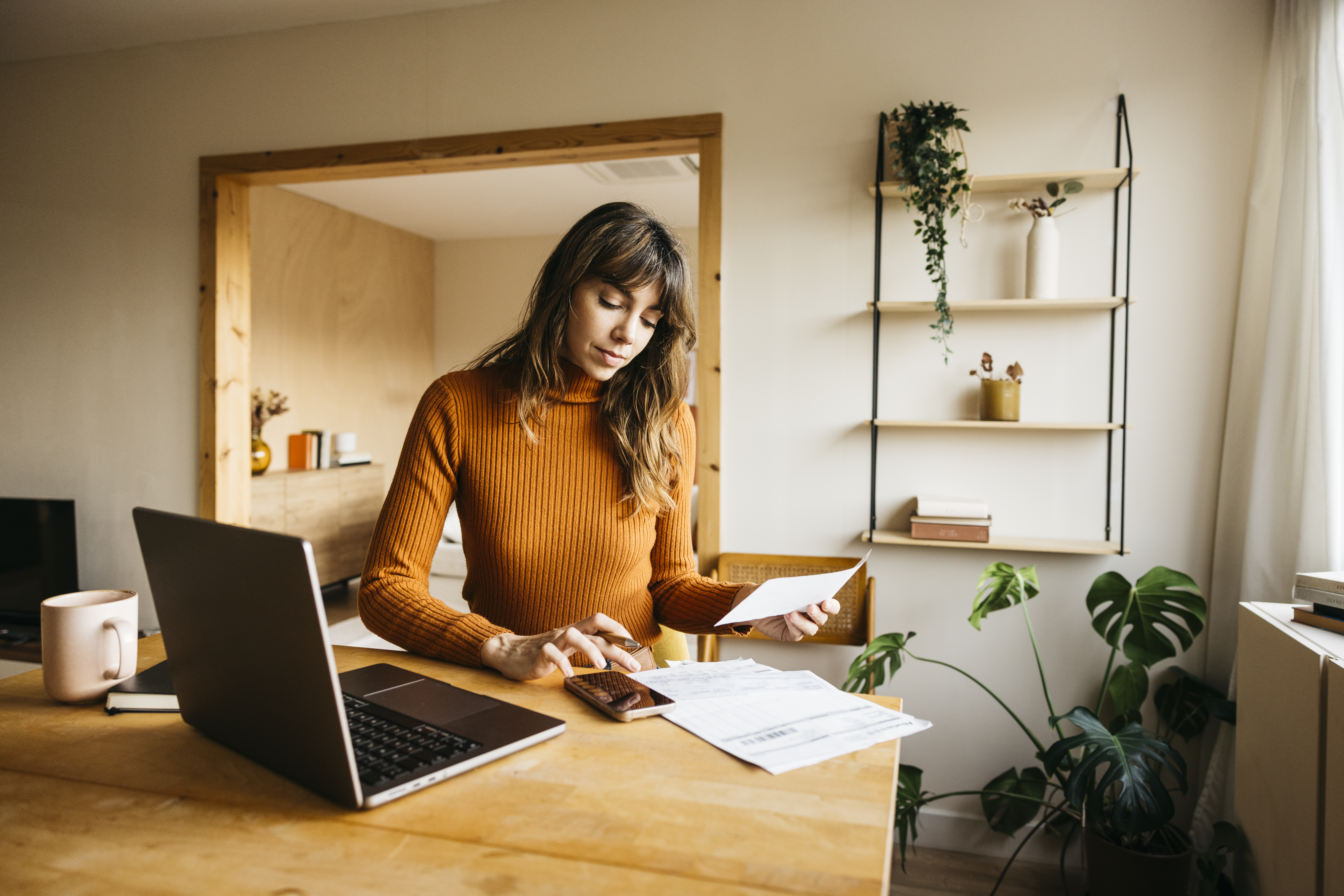 Woman calculating expenses using laptop and smartphone at a modern home office